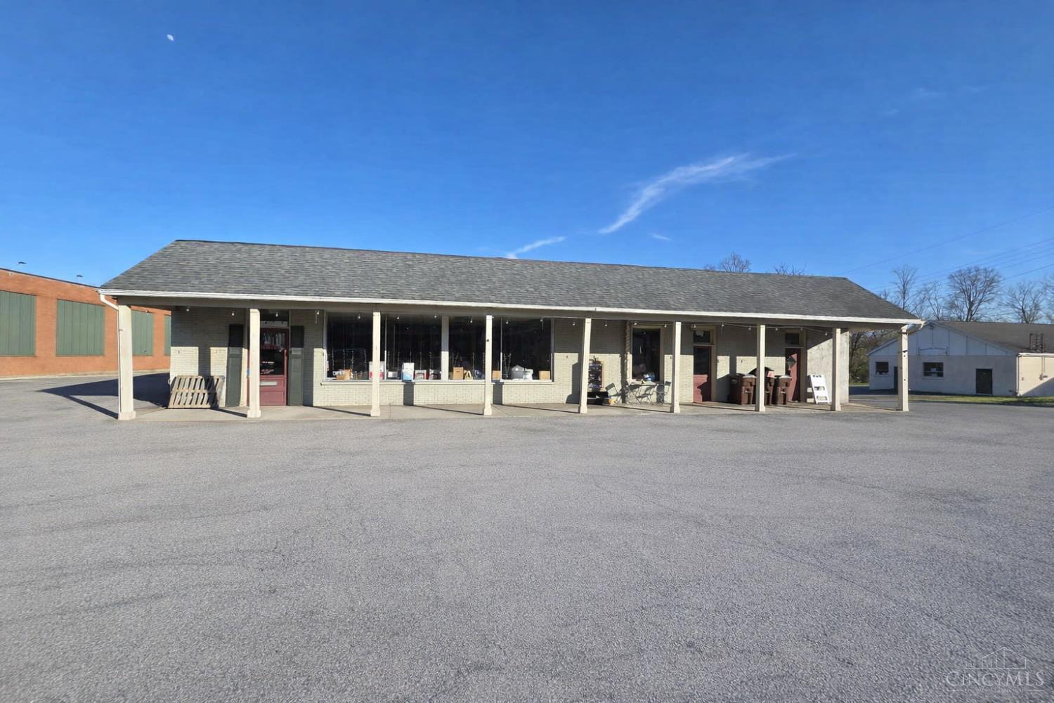 One-story storefront with a long covered porch, broad windows, and a large paved parking area.