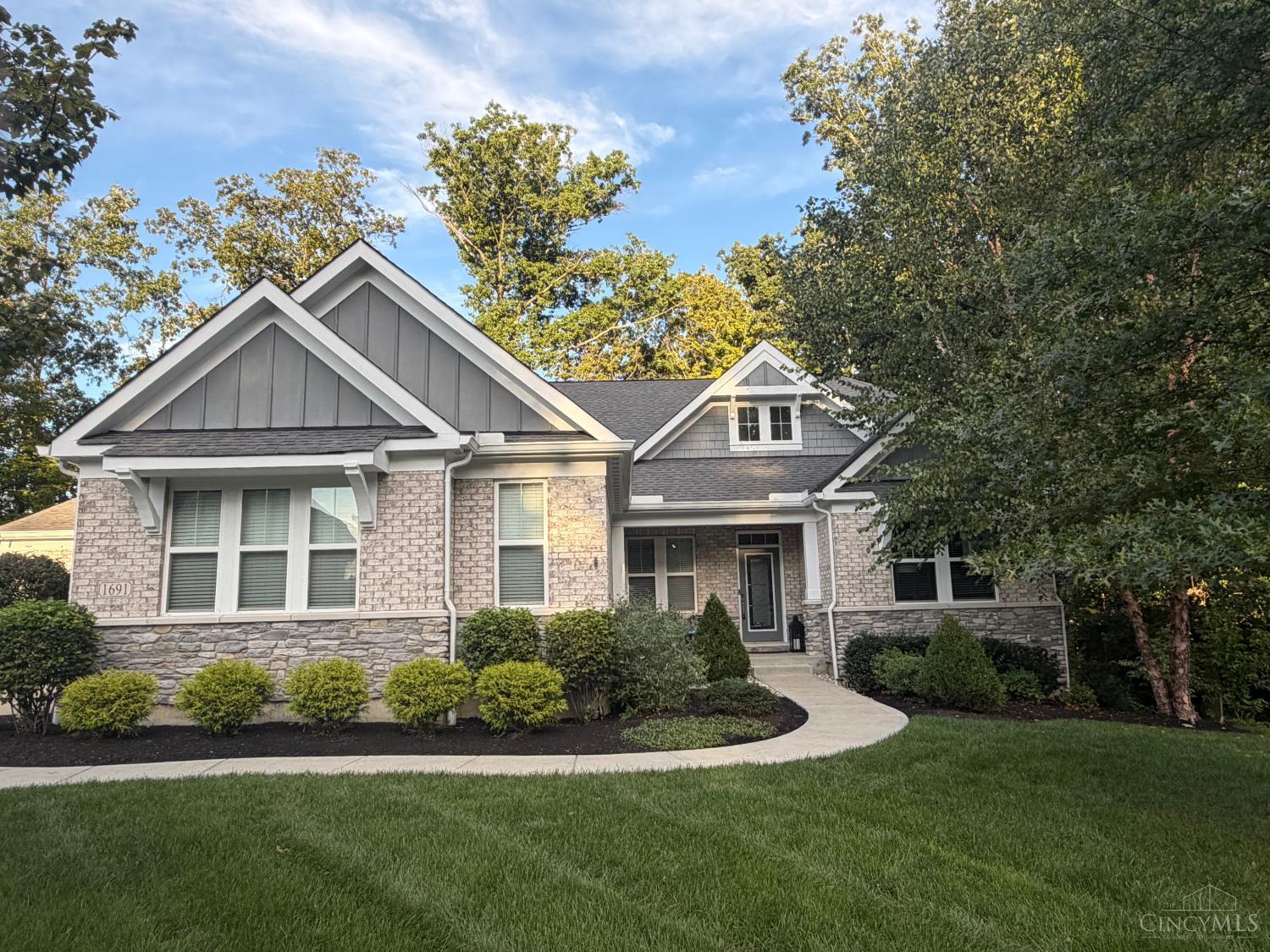 Gray-and-white brick-and-stone house with multiple gables, landscaped shrubs, and a curved front walkway.