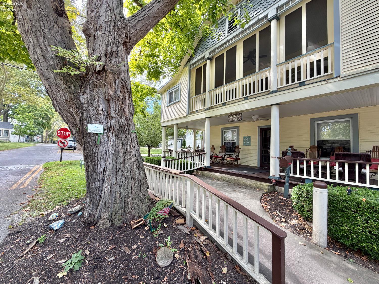 Two-story Lakeside building with a screened balcony and porch beside a massive tree.