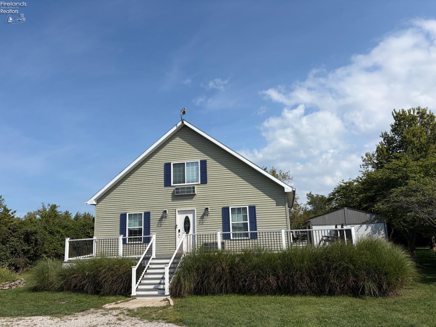 Gable-front house with blue shutters, white-railed steps, and ornamental grasses along the front.